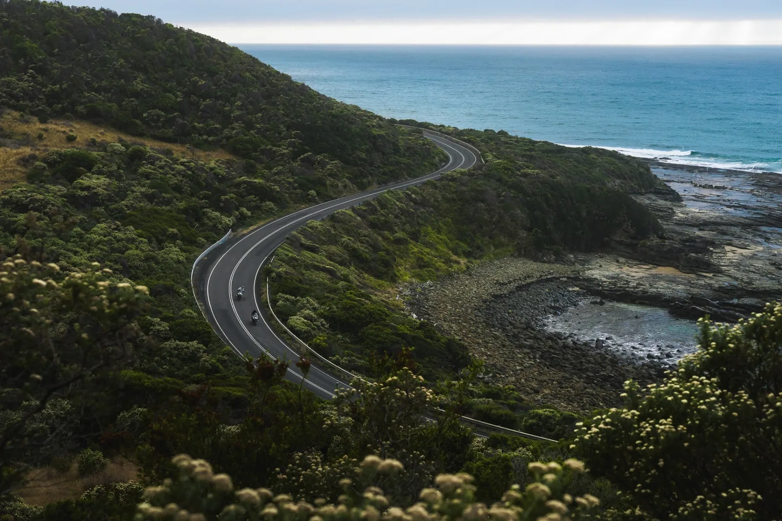 Two motorcycles riding on a winding coastal road above the Tasmanian coastline